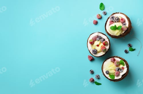 Preview: Coconut ice cream with fresh berries in coconuts halves on blue background with copy space. Top View