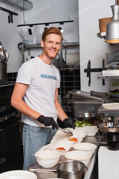 Preview: happy and redhead volunteer in latex gloves holding tweezers near plastic containers in kitchen