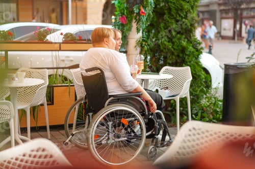 Preview: Woman with disability sitting in a wheelchair in outdoor cafe with her young daughter