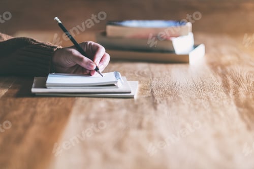 Preview: Closeup image of a woman writing on blank notebook on wooden table