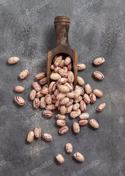 Preview: Wooden scoop full of dried pinto beans on gray top view. Traditional Latin American legumes