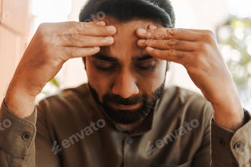 Preview: Tired, unhappy Indian businessman suffering from headache touching his temples, closeup
