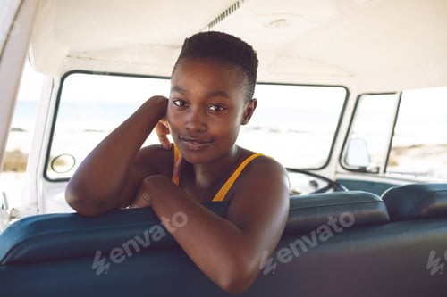 Preview: Front view of happy African american woman looking at camera while sitting in a camper van at beach