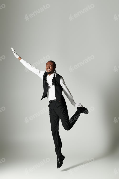 Preview: Young African American man in stylish suit striking an energetic pose against a grey backdrop