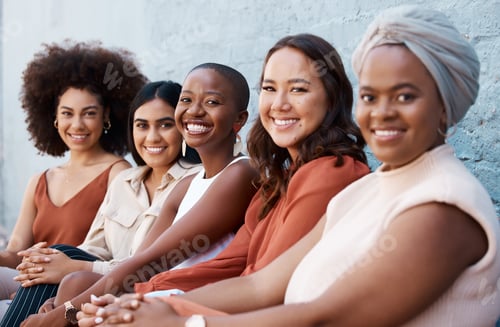 Preview: Group of diverse happy businesswomen sitting in a line with coworkers against a wall outside in the