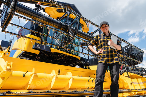 Preview: Female agricultural professional with tablet by combine harvester at equipment dealership