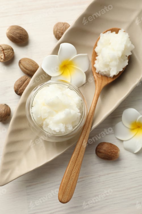 Preview: She butter, nuts and plumeria flowers on white wooden table, flat lay