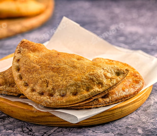 Preview: Freshly baked empanadas on a wooden plate.
