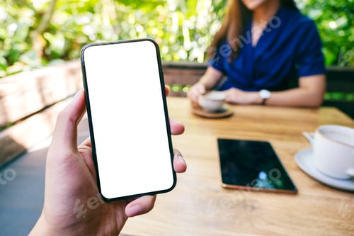Preview: A man holding black mobile phone with blank white screen with woman drinking coffee in cafe