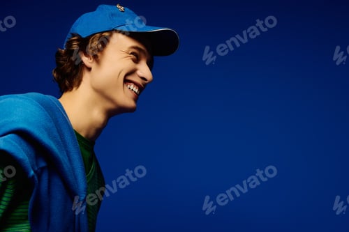 Preview: Young man showcases modern fashion style against vivid blue backdrop in lively atmosphere