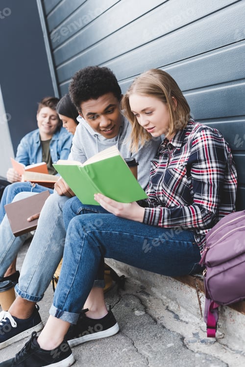 Preview: african american and caucasian teenagers sitting, talking and reading book