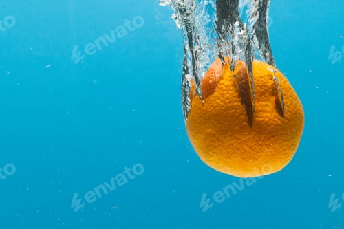 Preview: Close up of tangerine falling into water with copy space on blue background