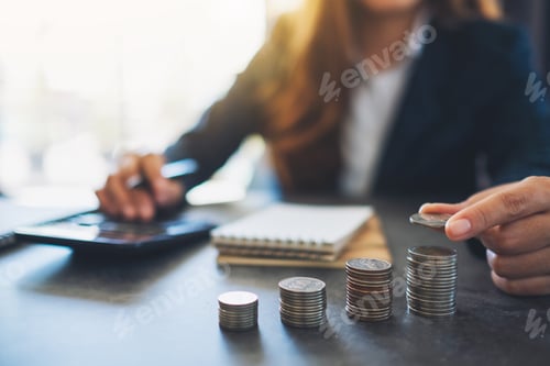 Preview: Businesswoman holding and stacking coins while calculating money on the table