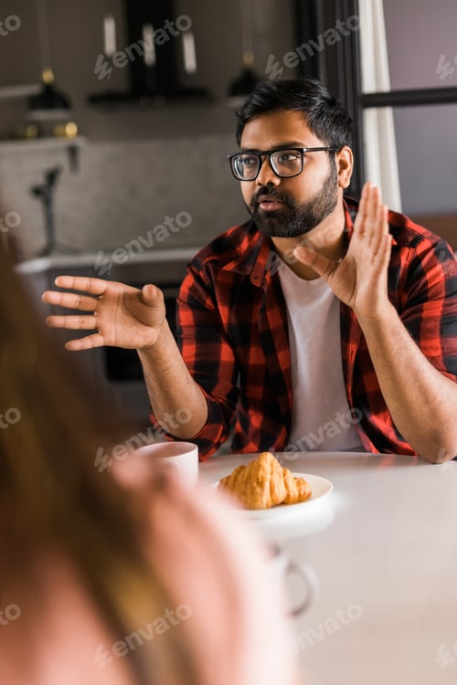 Preview: Happy indian couple having breakfast and small talk together in the kitchen - friendship, dating and