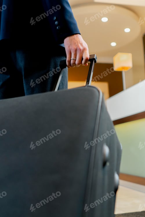 Preview: man arrived at the hotel during a business trip hand carries a suitcase on wheels close-up