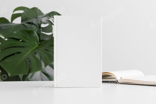 Preview: White book mockup with workspace accessories and a monstera plant.