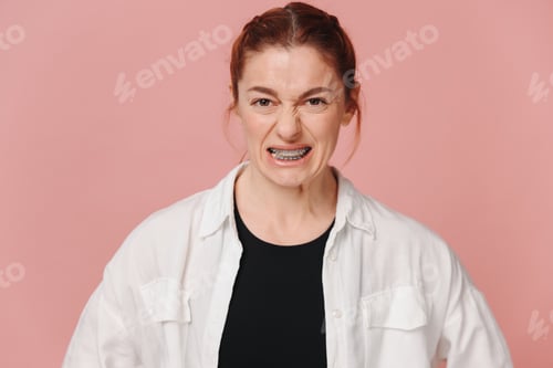 Preview: Portrait of red-haired mature woman suffering from pain due to braces on pink background