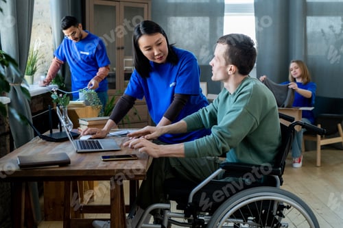 Preview: Asian woman in volunteer t-shirt helping disabled man