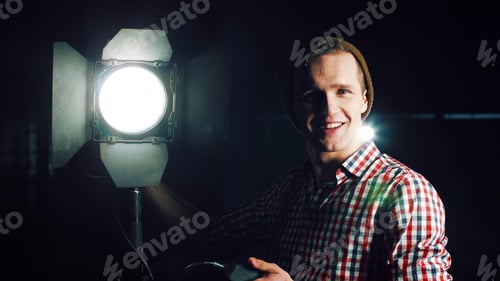 Preview: Stylish Man In Hat And Standing At Studio Light Stand With Switcher In Hand, Turning It On And