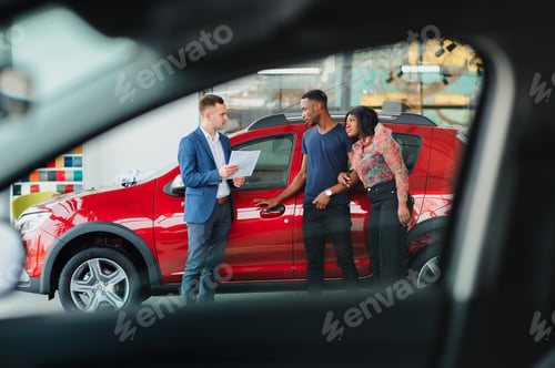 Preview: happy woman receiving a new car from her husband at dealership