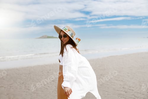 Preview: Cheerful young woman traveler with straw hat walking on tropical beach during vacation