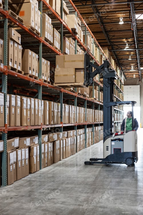 Preview: An employee picking products off a rack using a forklift stock picker in a distribution warehouse.