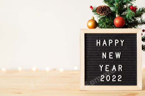 Visualização: Feliz ano novo 2022 saudações no quadro de cartas e na árvore de Natal com decorações de férias na mesa