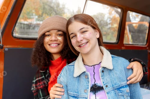Preview: Picnic in autumn nature. Two happy multiracial girlfriends sitting on car trunk in forest season