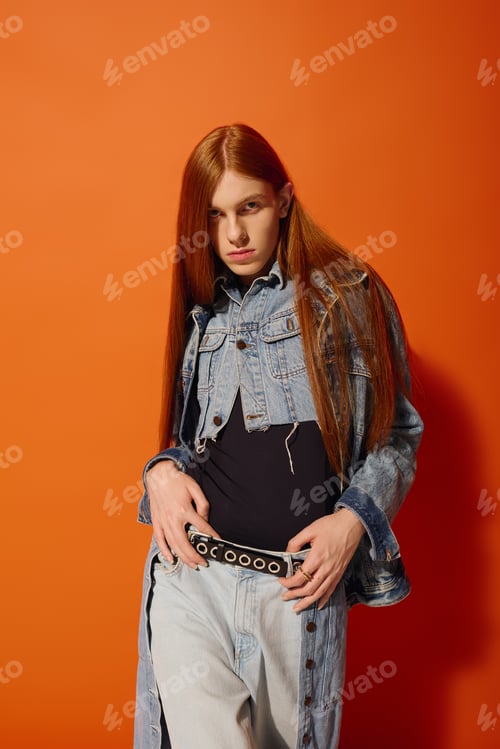 Preview: Emotional young man with long red hair poses confidently against a vibrant orange background