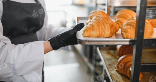 Preview: Baker placing tray of freshly baked croissants on rack in bakery