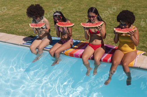 Preview: Diverse group of female friends eating watermelon sitting at the poolside