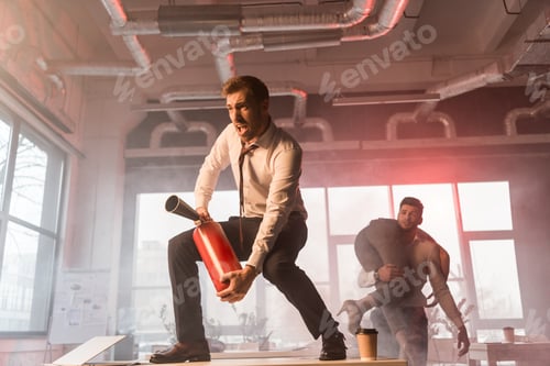 Preview: scared businessman screaming while holding extinguisher and standing on desk near coworkers in