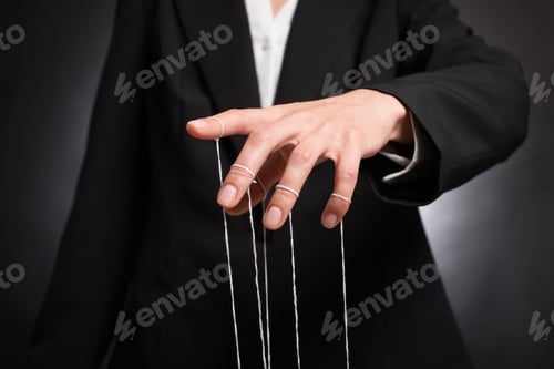 Preview: Woman in suit pulling strings of puppet on dark background, closeup