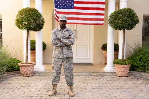 Preview: Portrait of confident male african american soldier standing with arms crossed against flag on house