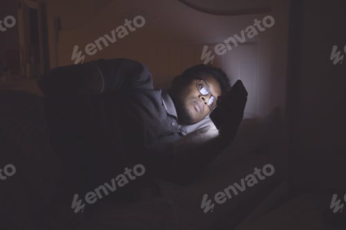 Preview: young man sitting on bed using smart phone at night