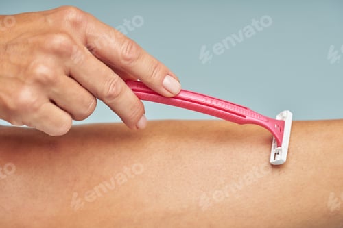 Preview: Close up of lady shaving her leg with safety razor isolated on blue background