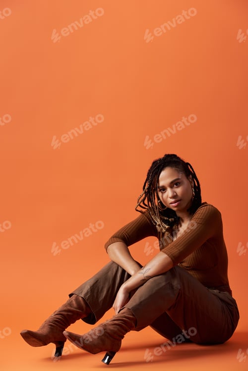 Preview: Stylish young African American woman with braids poses gracefully in a vibrant studio setting