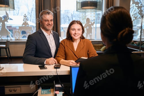 Preview: Caucasian couple looking at female reception desk during check-in in hotel lobby