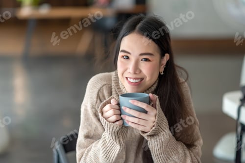 Preview: Beautiful young Asian woman relaxing at home drinking coffee wearing long sleeves. at the camera.