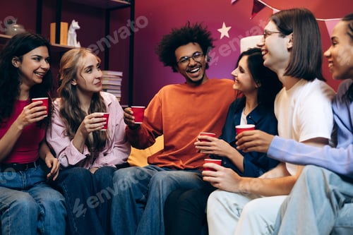 Preview: Diverse group of multinational young adults laughing and socializing at party in modern living room