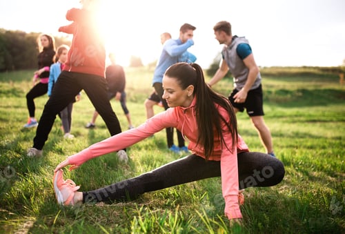 Preview: Large group of fit and active people doing exercise in nature, stretching.