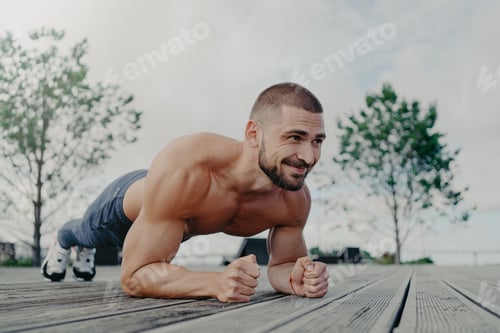 Preview: Shirtless determined bearded man with naked torso stands in plank pose and smiles gladfully