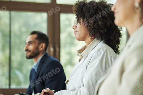 Preview: Young Black Woman in White Coat Listening Attentively during Medical Meeting