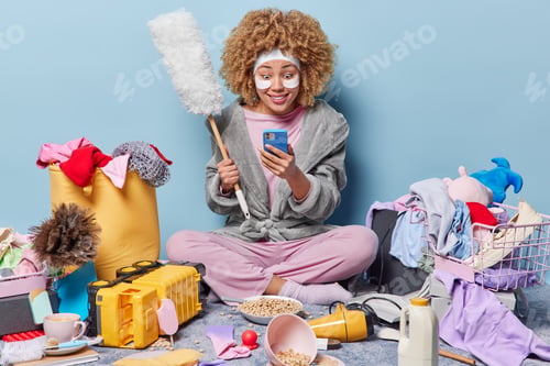 Preview: Housekeeping. Impressed woman stares at smartphone screen reacts to shocking news holds dusting