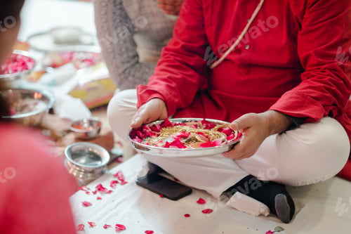 Preview: Indian man sitting in the lotus position holding a bowl filled with gold jewelry