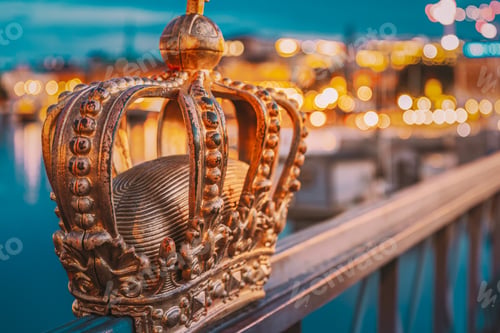 Preview: Stockholm, Sweden. A gold crown on railing by waterside, surrounded by urban elements