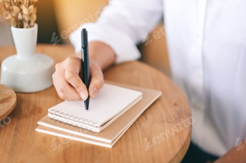 Preview: Closeup image of a woman writing on a blank notebook on wooden table