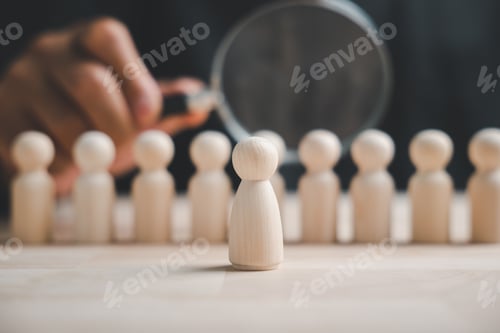 Preview: A single wooden figurine stands out from a row of similar figures, highlighted by a magnifying