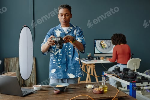 Preview: Young Adult Black Man Adjusting Camera While Photographing Food in Studio