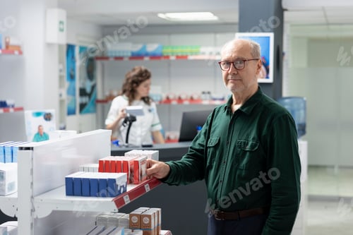 Preview: Portrait of happy retired man searches for wellness pills during pharmacy visit